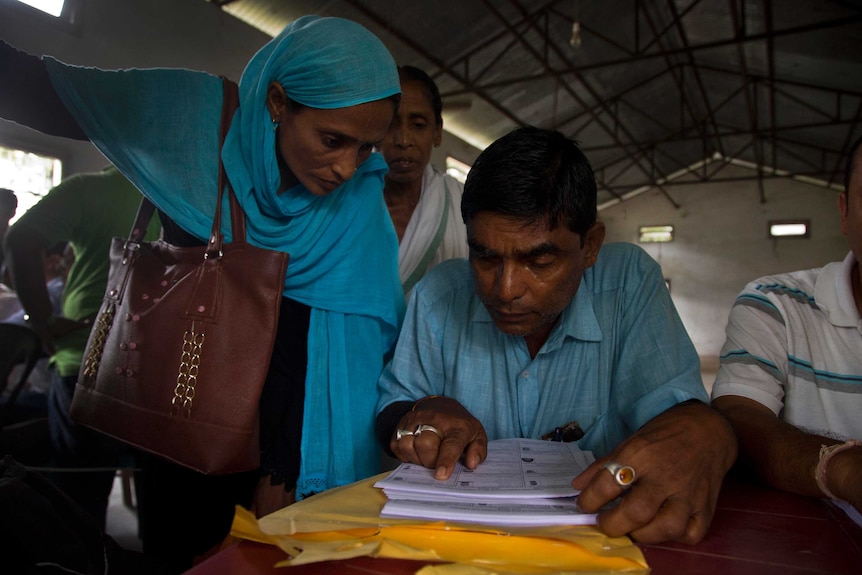An Assam Muslim woman in a blue headscarf and a man in blue shirt check their names on the NRC list