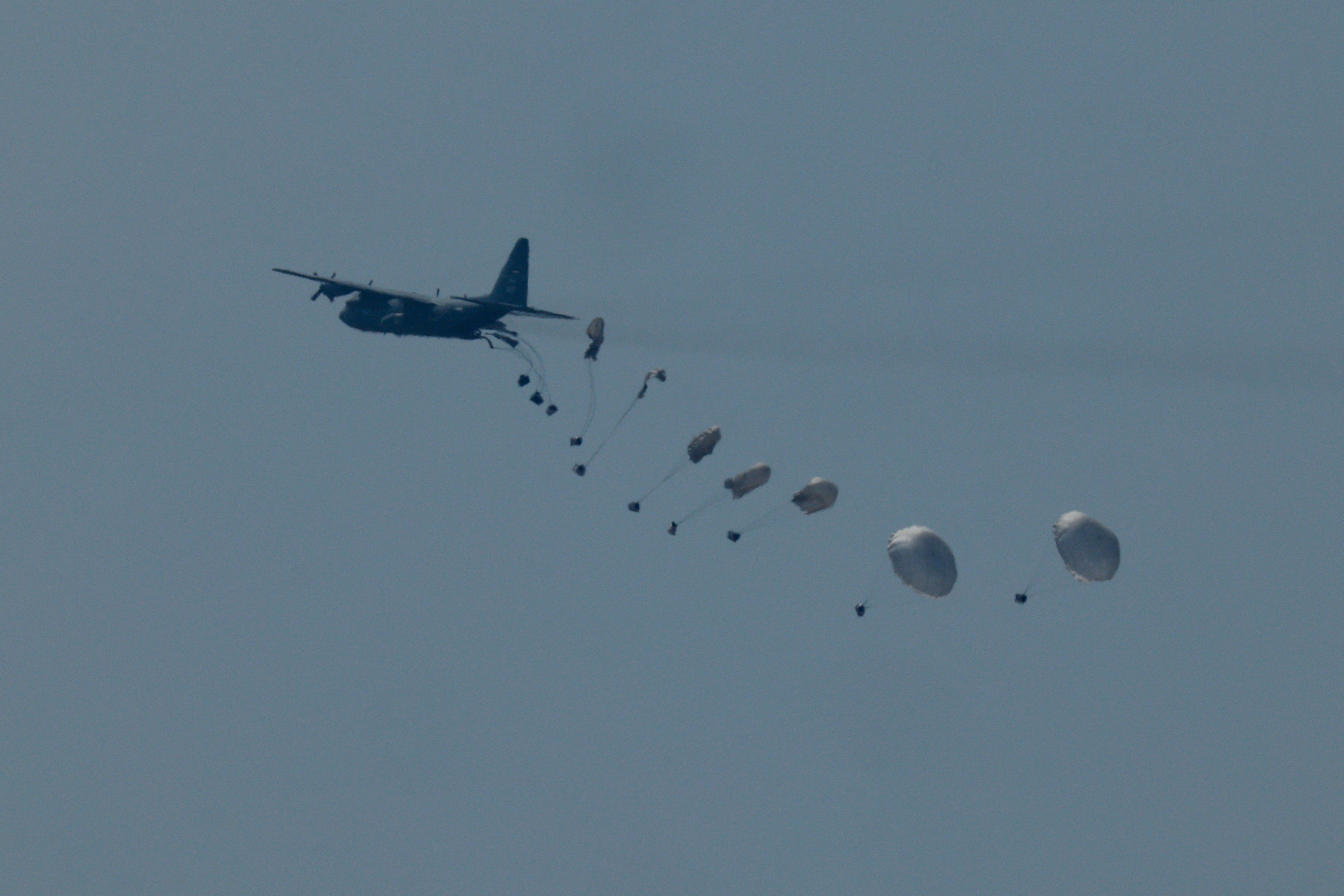 A large military plane with multiple boxes of supplies parachuting down behind it.