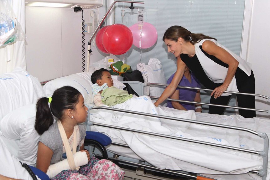 Spain's Princess Letizia leans over a hospital bed to speak to an injured boy wearing a cast on his arm.