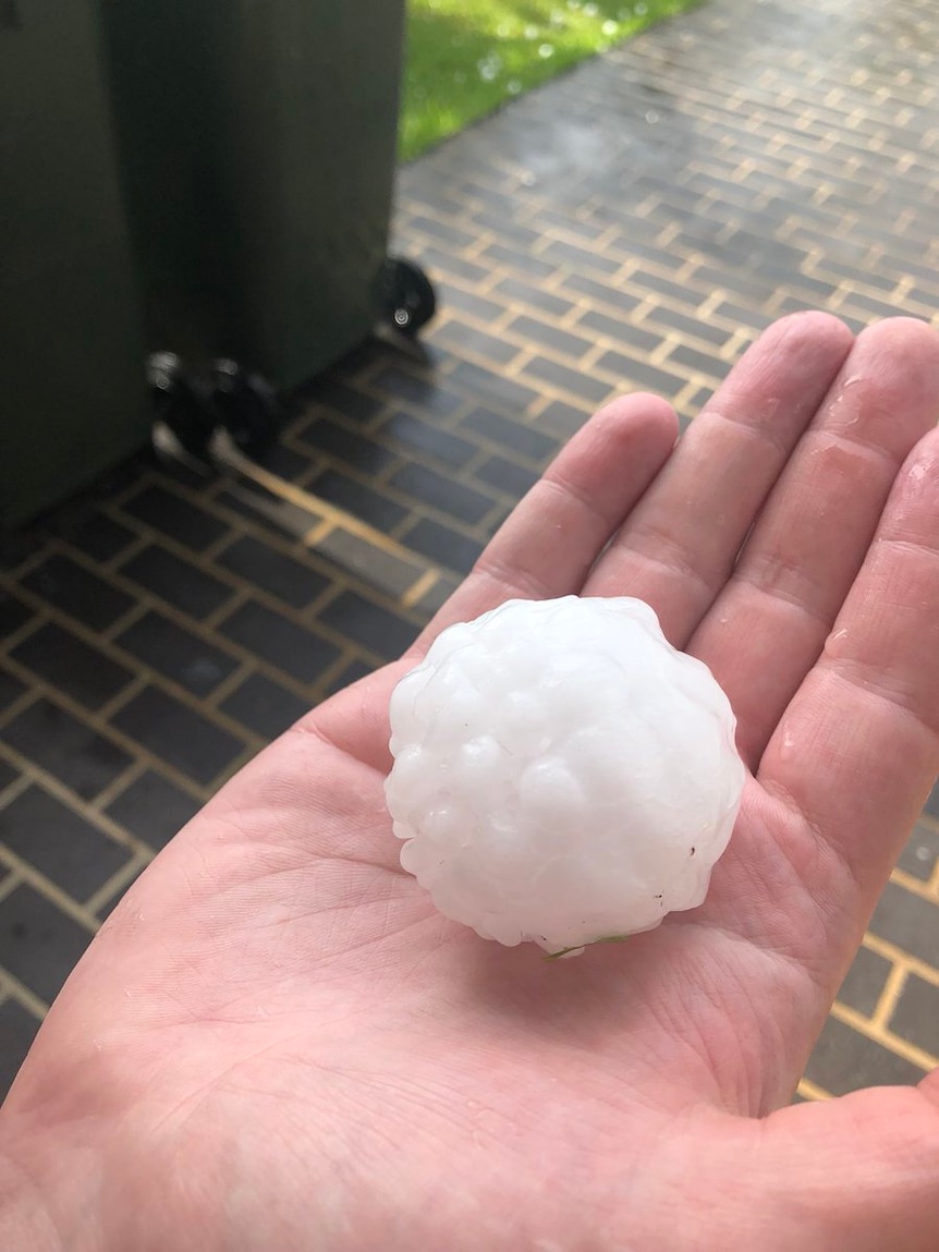 A large hailstone is held in the palm of a woman's hand.