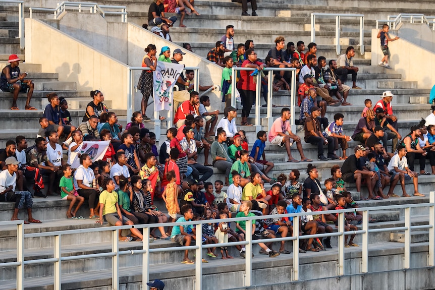 Fans of a soccer team sit on concrete benches inside a sporting stadium.
