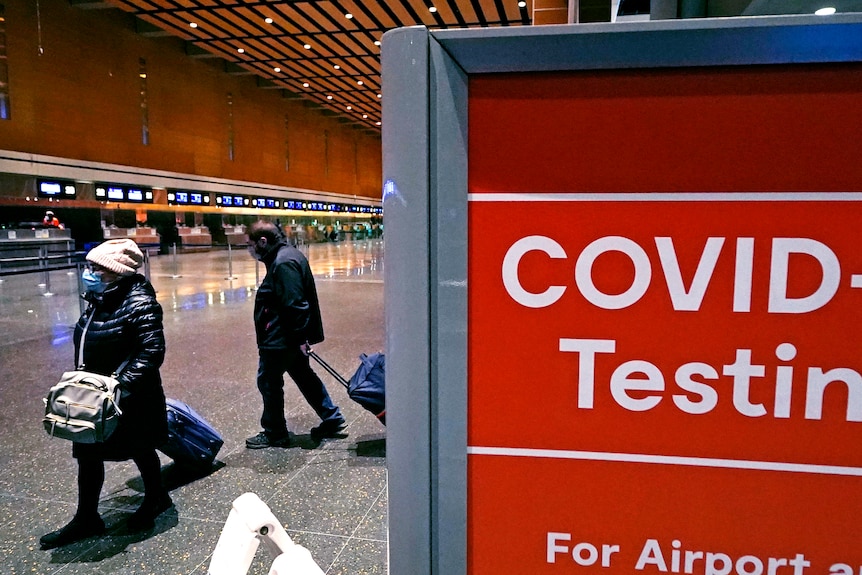 Travelers pass a sign near a COVID-19 test site in Terminal E at Logan Airport.