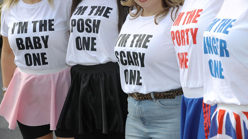 Close-ups on a group of women show their T-shirt slogans read "I'm the Baby/Posh/Scary/Sporty/Ginger one"
