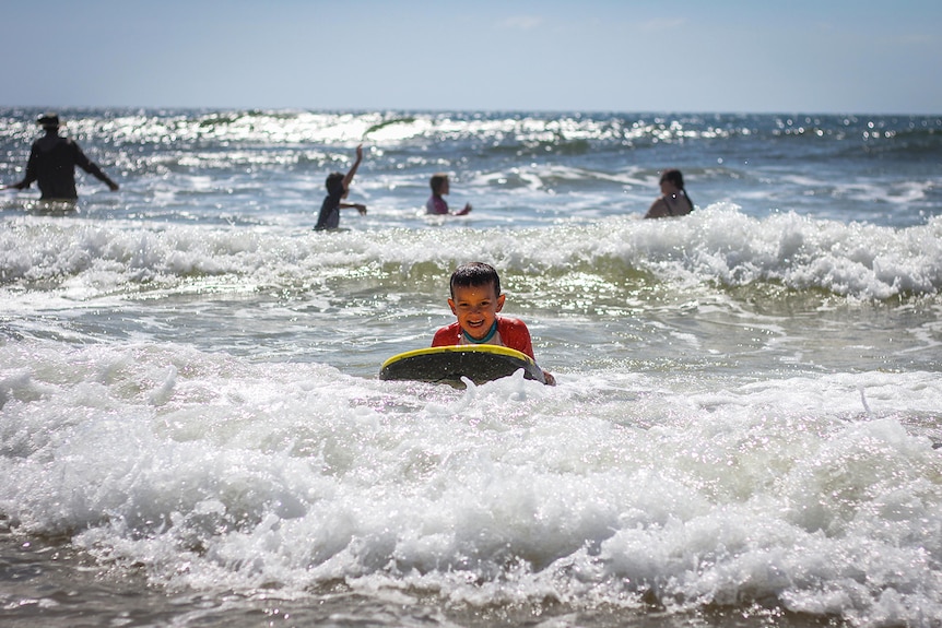 Primary school boy from outback Queensland on a boogie board in the surf at Rainbow Beach