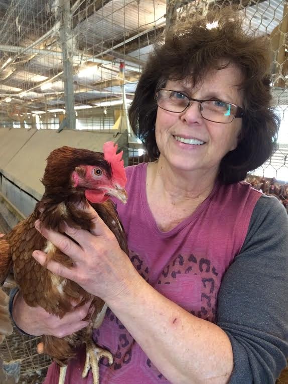 A woman smiles and holds a chicken close to the camera.