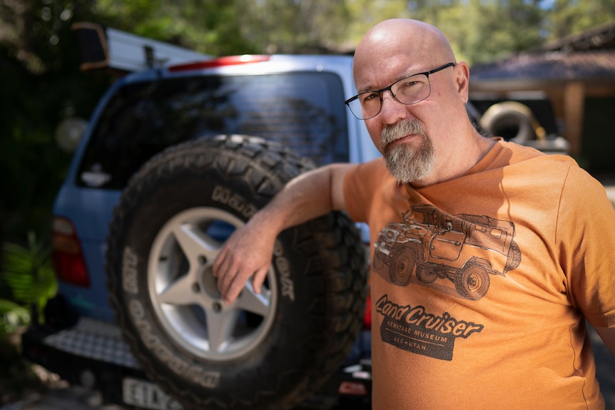 Man wearing an orange shirt standing next to a 4WD. 