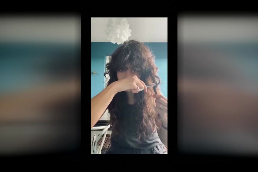 A still from a video of a woman cutting her hair. 