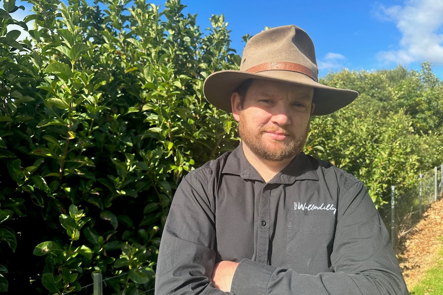 Man stands outside wearing a hat with his arms folded 