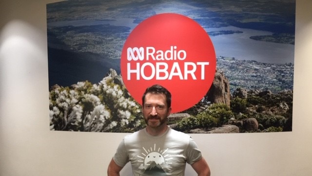 Stroke survivor Matt Picone stands in front of ABC Radio Hobart sign showing a picture of the pinnacle of kunanyi/Mt Wellington