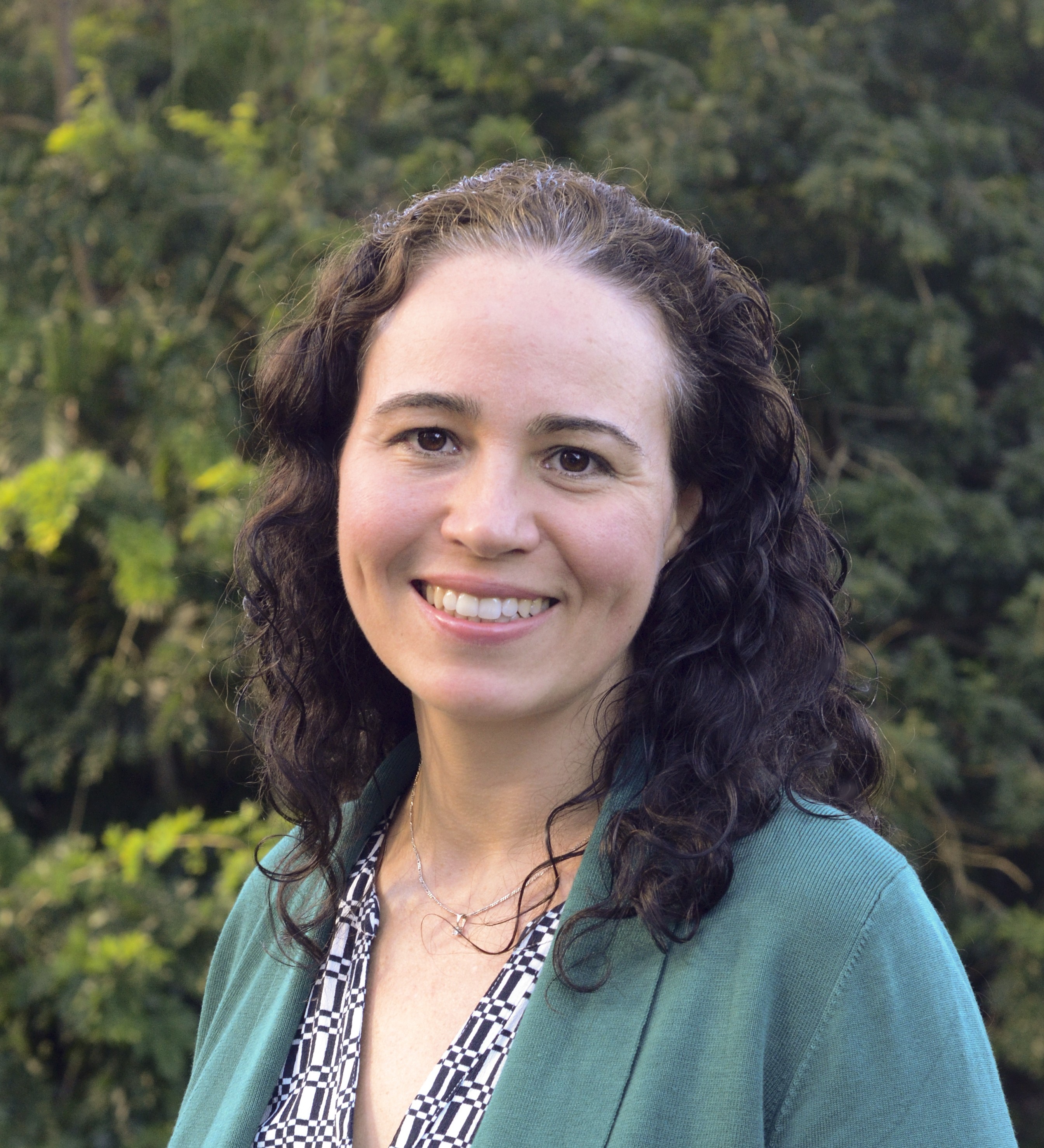 A woman smiling to the camera with trees in the background