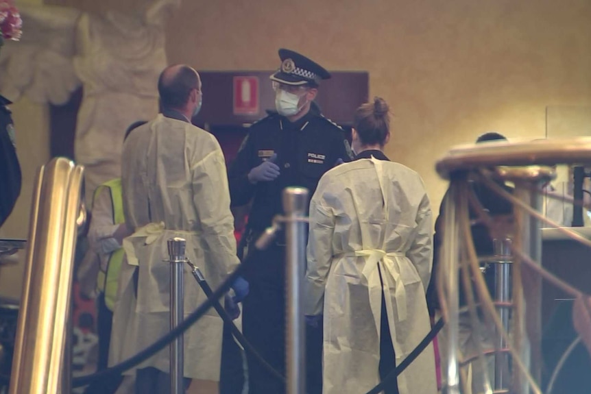 A police officer wearing a face mask speaking to two people wearing white hospital gowns