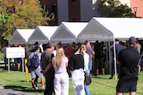 A crowd of people with most wearing facemasks stands near a white canopy outside Royal Perth Hospital.