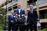 Four men in suits at a media conference. 