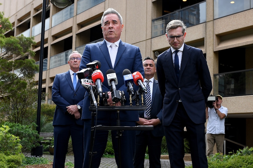 Four men in suits at a media conference. 