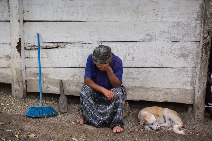 Grandmother of deceased Guatemalan migrant, Jakelin Caal lays her head in her hands while a dog sits curled next to her