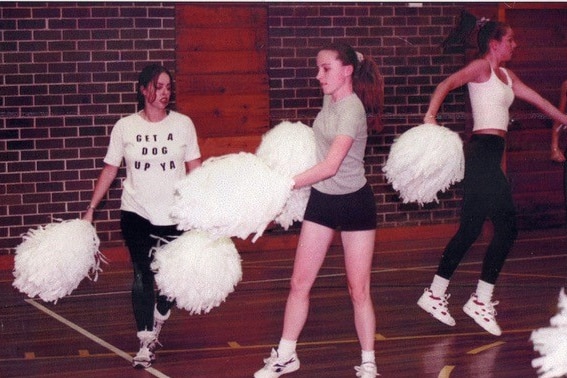 Young women in casual clothes practising cheerleading with pom poms.