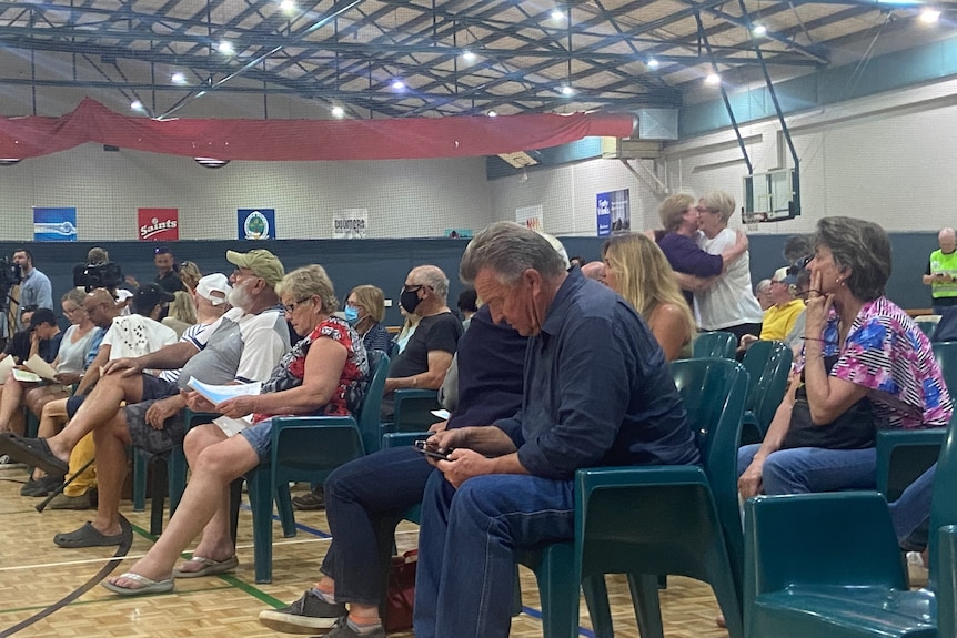 Several dozen people sitting in rows of chairs in a community centre.