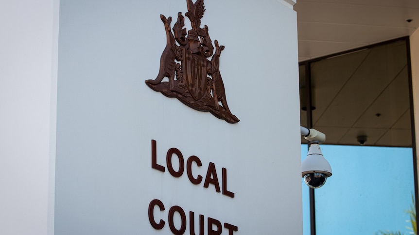 A coat of arms and sign saying 'Local Court' on a column outside a courthouse. 