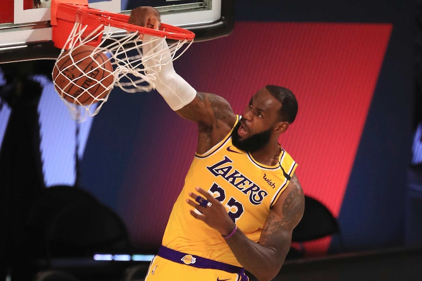 LeBron James has his mouth open as he slams the ball through the hoop, jumping above a number of other players