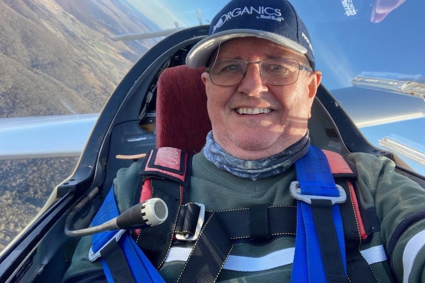 Smiling man in glasses and cap inside glider, with ground visible behind