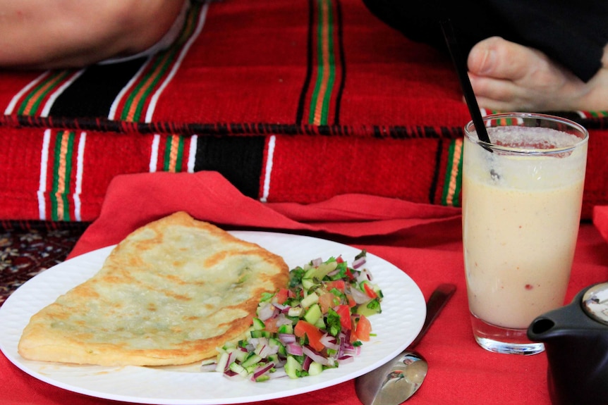 A plate with Afghan bread and salad sits on the ground beside a drink