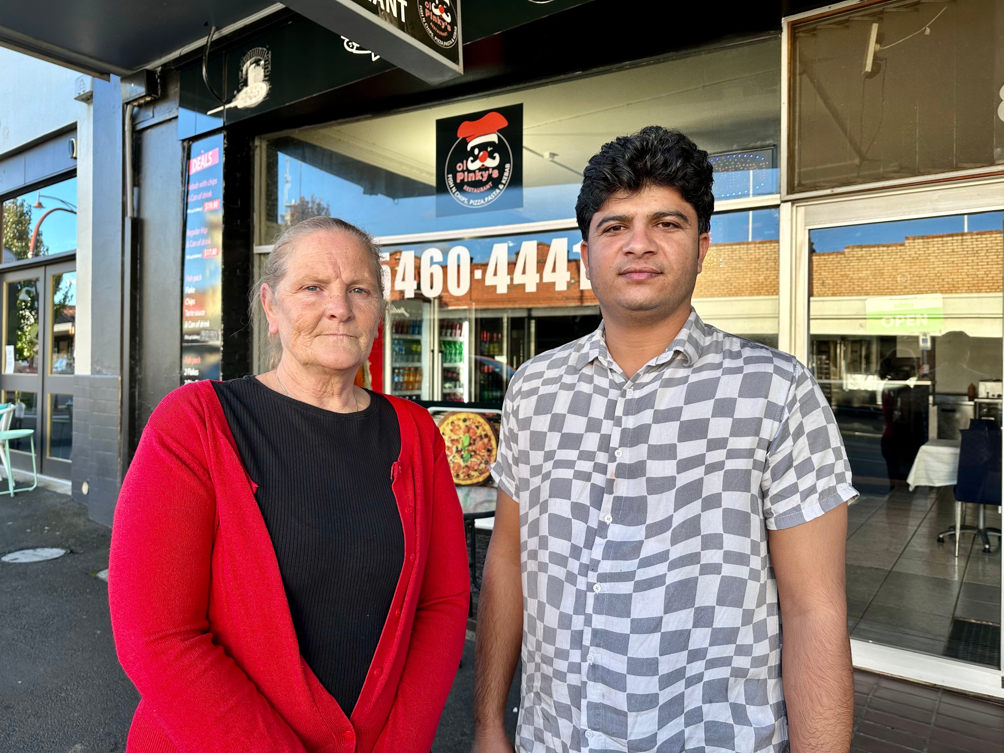 Two people standing in front of a pizza store, with the logo visible in the background.