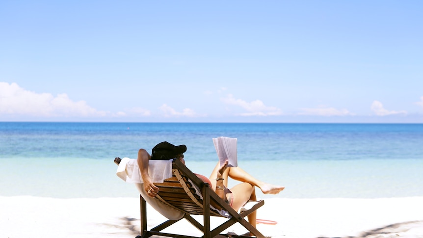 Woman reclined in chair reading a book on a beach