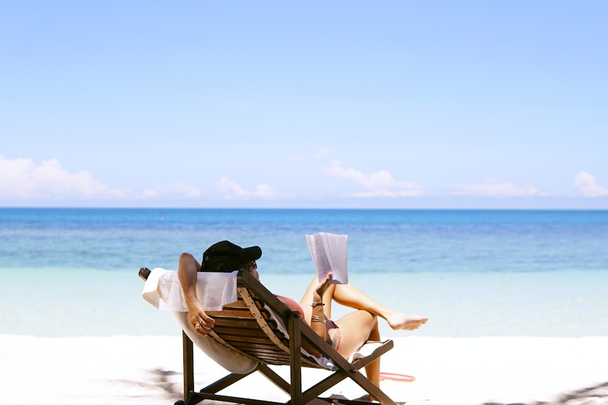 Woman reclined in chair reading a book on a beach