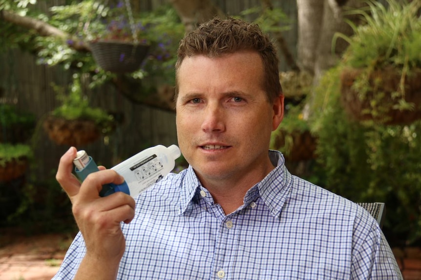 A young man holds a ventolin inhaler and spacer.