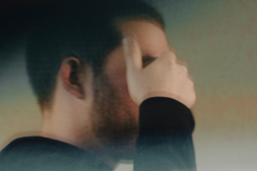 A blurred photo of a man's face in profile. His hand is shielding his eyes
