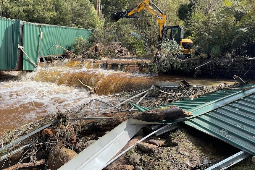 Flood water washes past buildings with machinery in the background