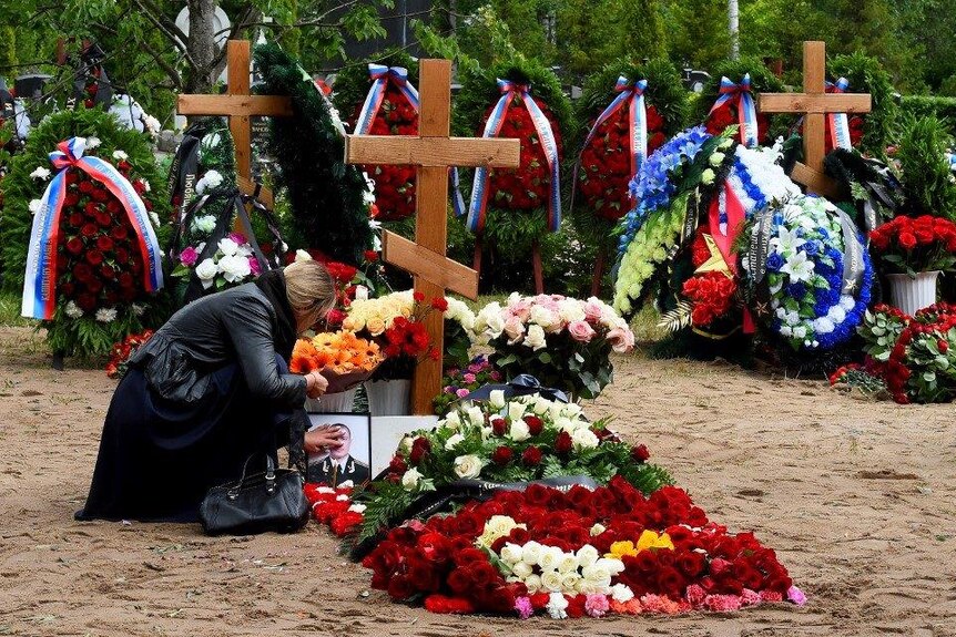 A woman touches a photo of a dead Russian officer with a cross in the background and flowers laid over the fresh grave.