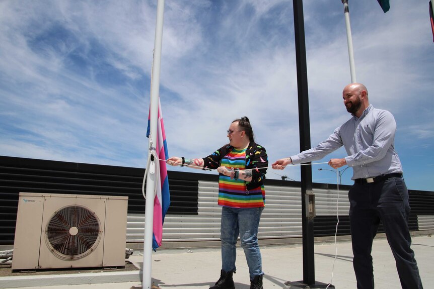 Two people hoist a Transgender Pride flag on a roof