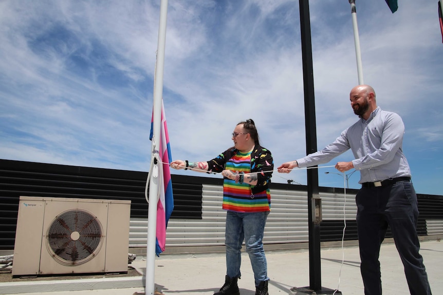 Two people hoist a Transgender Pride flag on a roof