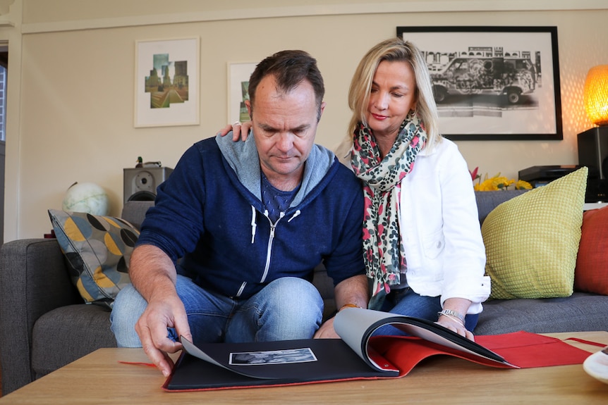 Couple sitting on the couch, flicking through a photo album.