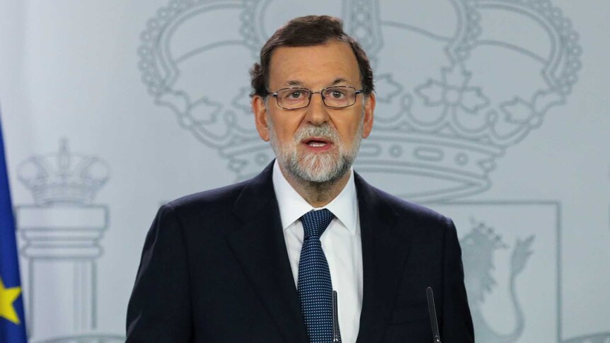Spanish Prime Minister Mariano Rajoy stands in front of a podium and next to a Spanish flag.