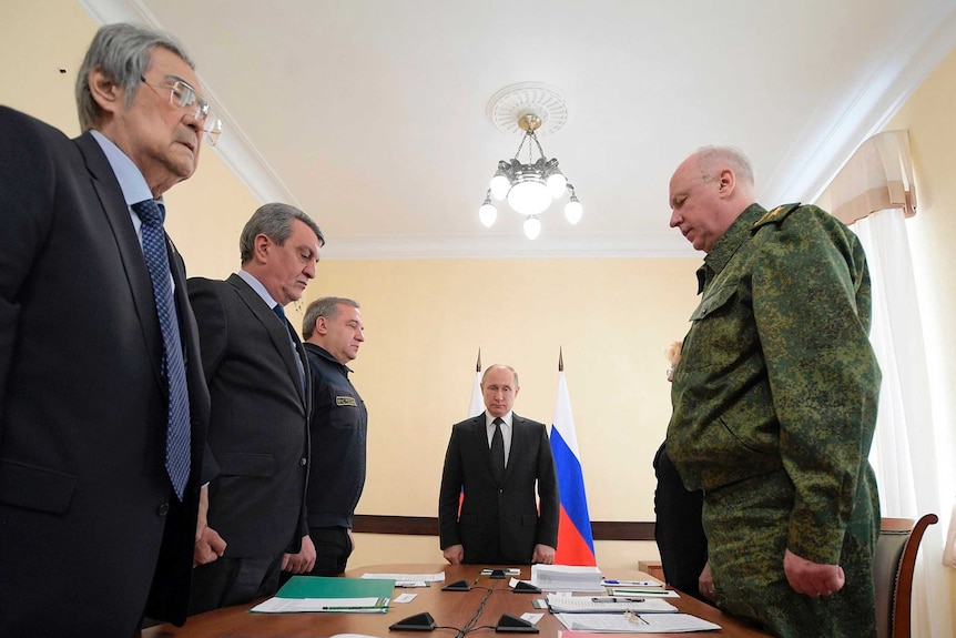 Vladimir Putin and local officials stand in a meeting room to commemorate the victims of the shopping centre fire.
