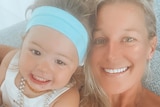 A toddler wearing a blue headband and pearl necklaces next to her mum. Both are smiling. 