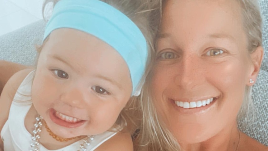 A toddler wearing a blue headband and pearl necklaces next to her mum. Both are smiling. 