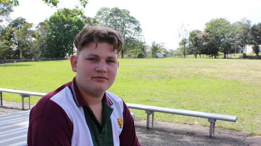 Macksville Highschool student sitting at a bench with sports oval in the background.
