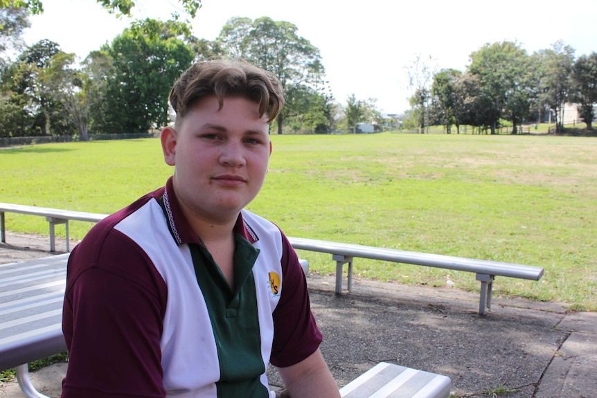 Macksville Highschool student sitting at a bench with sports oval in the background.