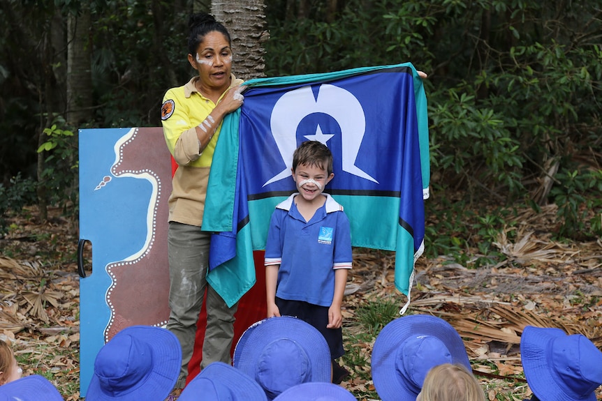 A boy stands in front of the Torres Strait Islander flag held by Delta Kay.