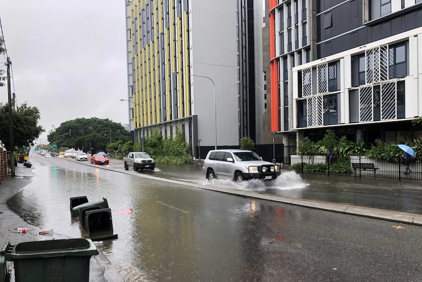 Flooded northbound lanes of Vulture Street at South Brisbane. A couple of vehicles are driving through low water.