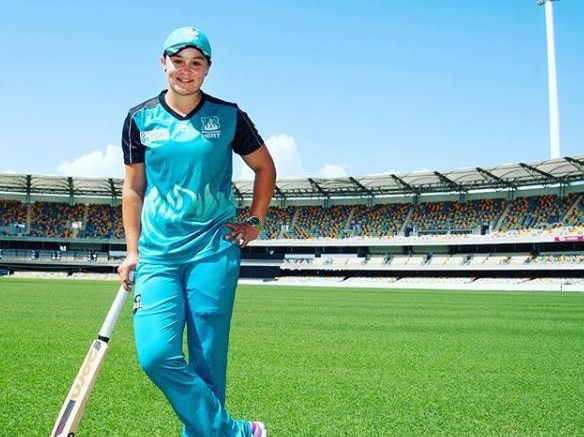 Ash Barty on a cricket pitch holding a bat.