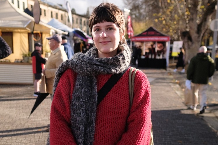 A young woman in a red junmper stands at an outdoor market