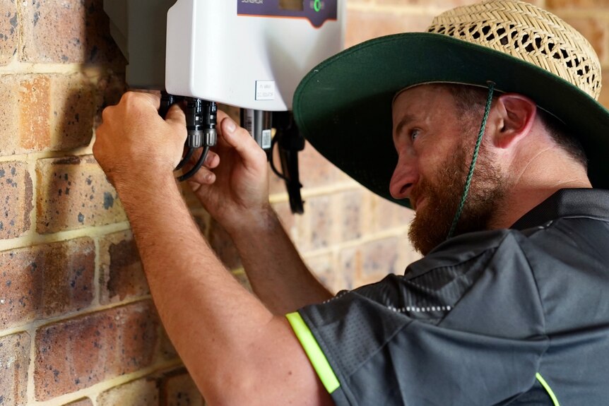 A man attaches a solar power wall unit to a brick garage wall