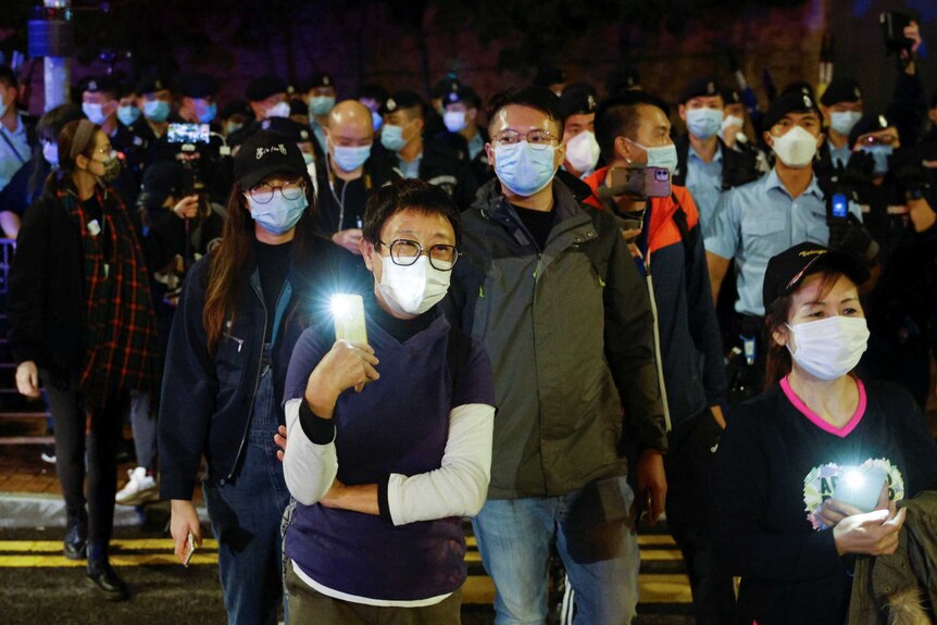 A group of people wear masks at night holding flashlights in their hands to show support for Hong Kong's pro-democracy activists