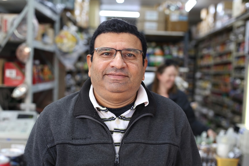 William D'Souza stands in front of rows of shelves of supplies at his Preston Market stall.