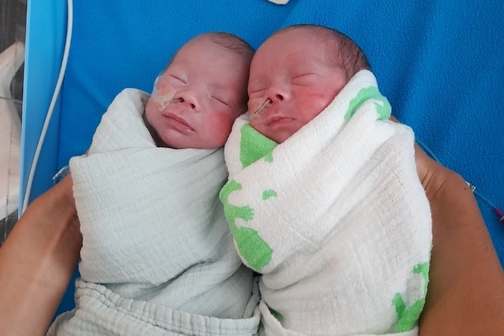 Two babies sleeping side by side, wrapped tightly in blankets, with tubes coming out of their noses. 