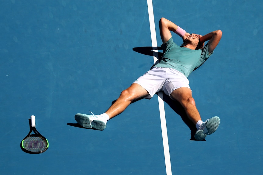 Stefanos Tsitsipas lies on the court with his hands on his head celebrating his win over Roberto Bautista Agut.